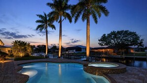 A swimming pool with a tiled edge, surrounded by palm trees and a brick walkway. - Boater’s Paradise in SW Cape Coral | Coastal Retreat with Pool, Spa, Dock & Tropical Outdoor Oasis (Cape Coral)