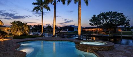 A swimming pool with a tiled edge, surrounded by palm trees and a brick walkway.