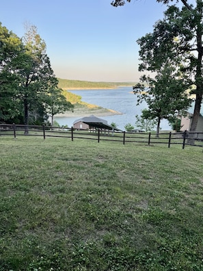 A grassy area with a wooden fence, a covered structure, and a view of a lake.