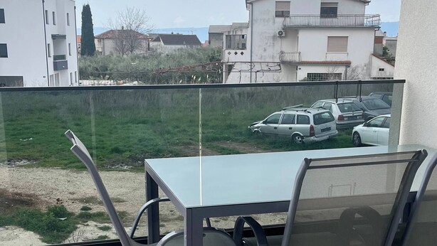 Un balcon avec une table et des chaises, donnant sur des voitures garées et sur des bâtiments en arrière-plan.