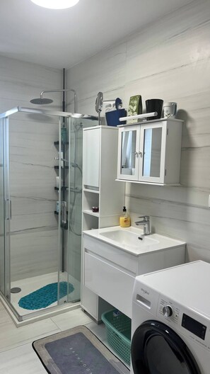Ein modernes Badezimmer mit Duschkabine aus Glas, Waschbecken mit Spiegel und einer Waschmaschine.