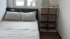 Une chambre à coucher comprenant un lit, une fenêtre, une table de chevet avec une lampe et une petite étagère sur laquelle est posé un objet décoratif.