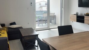 Un salon moderne avec une table à manger en bois, des chaises noires, un canapé et une porte-fenêtre coulissante donnant sur un balcon.