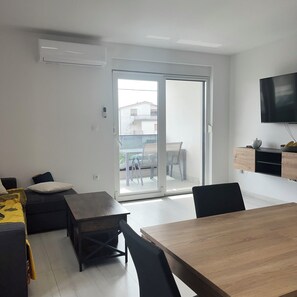 Ein modernes Wohnzimmer mit einem Holzesstisch, schwarzen Stühlen, einer Couch und einer Glastür, die auf einen Balkon führt.