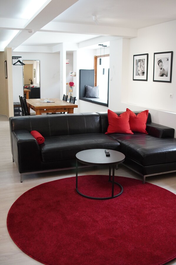A modern living room with a black leather sofa, red cushions, a round coffee table, and a red rug.