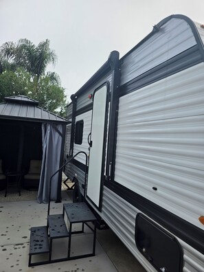 A travel trailer with a covered patio area, a step-up platform, and a door.
