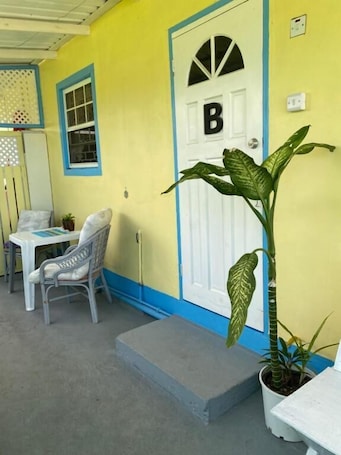 A yellow building with a white door marked with a large 'B', a small table with chairs, and a potted plant.