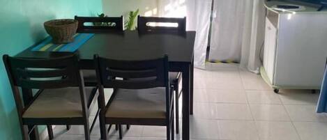 Un comedor con una mesa y sillas, un reloj en la pared, un televisor sobre un mueble bajo y una cortina.