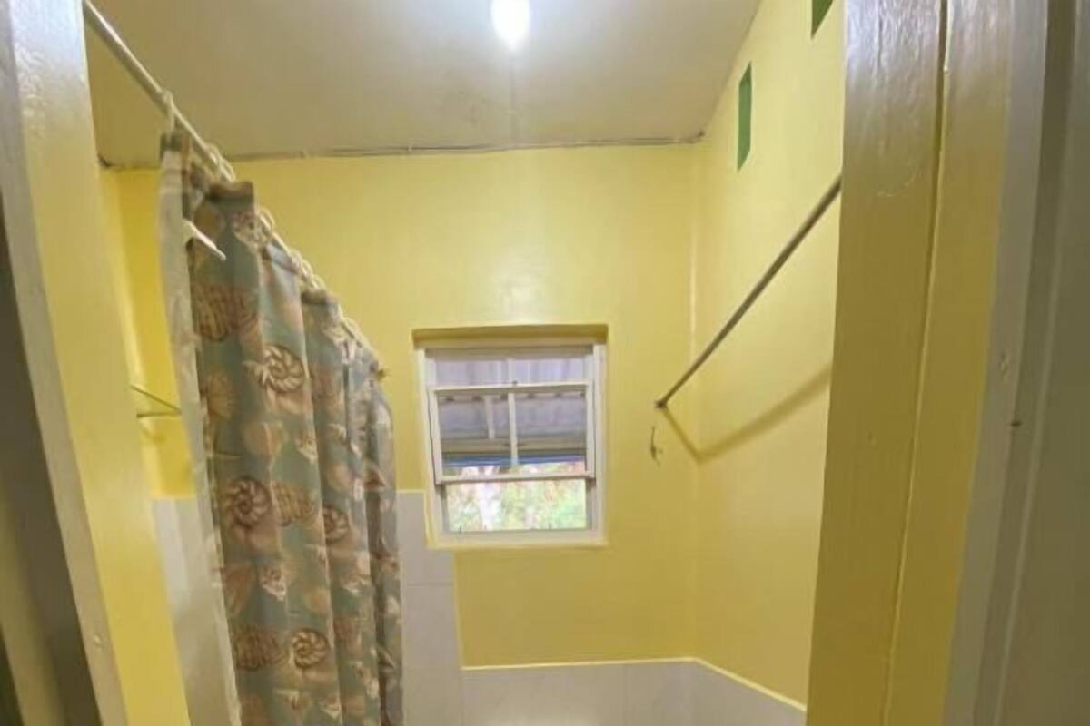 Un baño pequeño con inodoro, ventana, cortina de ducha y un tapete.