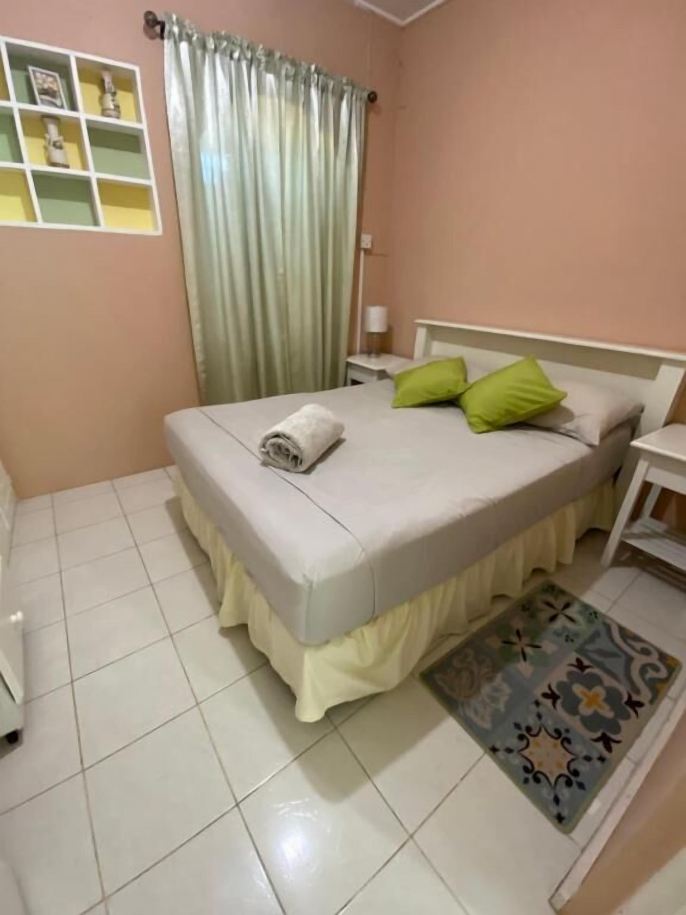 Quarto com cama, mesa de cabeceira, luminária, prateleira com objetos decorativos e tapete estampado.