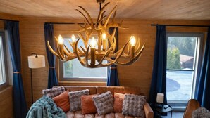 Een gezellige kamer met een leren bank, een kroonluchter met een gewei-achtig ontwerp, en uitzicht op het landschap door een raam.