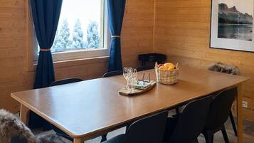 Um interior de madeira com uma mesa de jantar, cadeiras, uma cesta de frutas e uma moldura na parede.