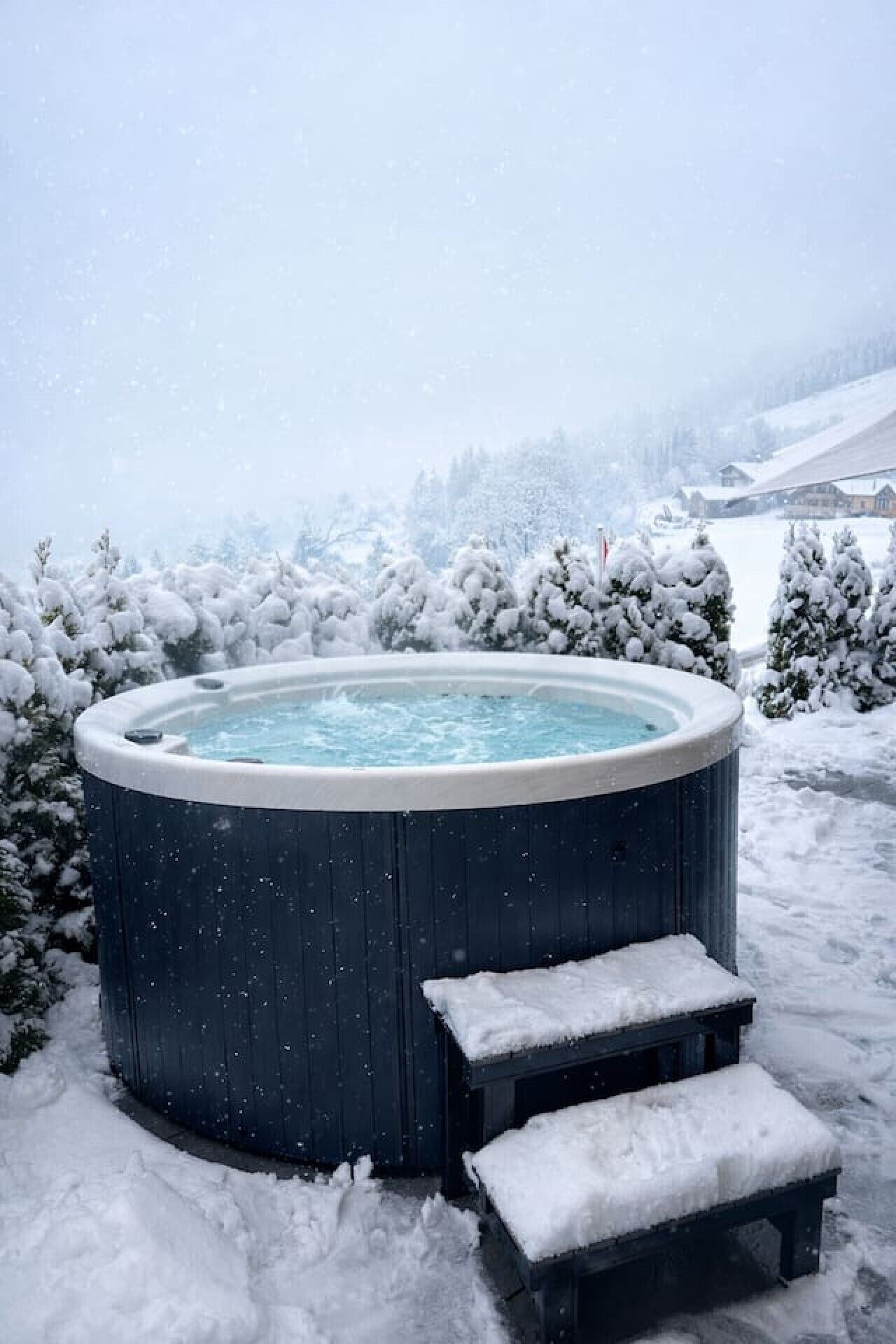 Un bain à remous installé à l’extérieur, dans un décor enneigé, avec des marches menant à l’accès.