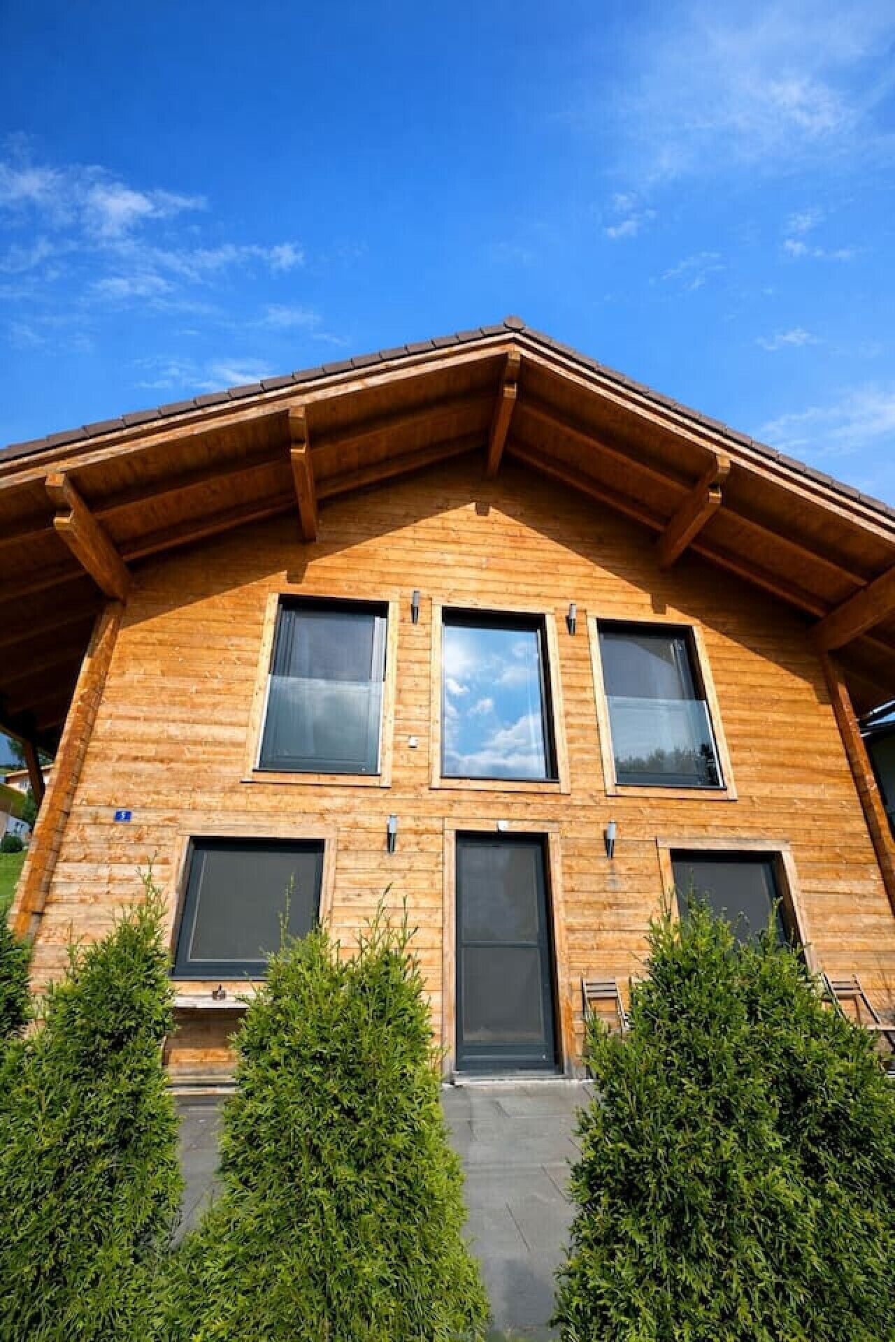A modern wooden building with a sloped roof, multiple windows, and a front entrance.