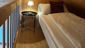 Een kleine, knusse kamer met een enkel bed, een nachtkastje en een lamp.