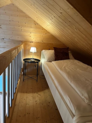 A small, cozy room with a single bed, a nightstand, and a lamp. - Modern SPA Chalet near Interlaken • AC • Hot Tub by SwissDreamLiving (Beatenberg)