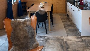 Een gezellig interieur van een chalet met houten plafond, een eethoek met tafel en stoelen, een keuken met moderne apparatuur, en een raam met gordijnen.
