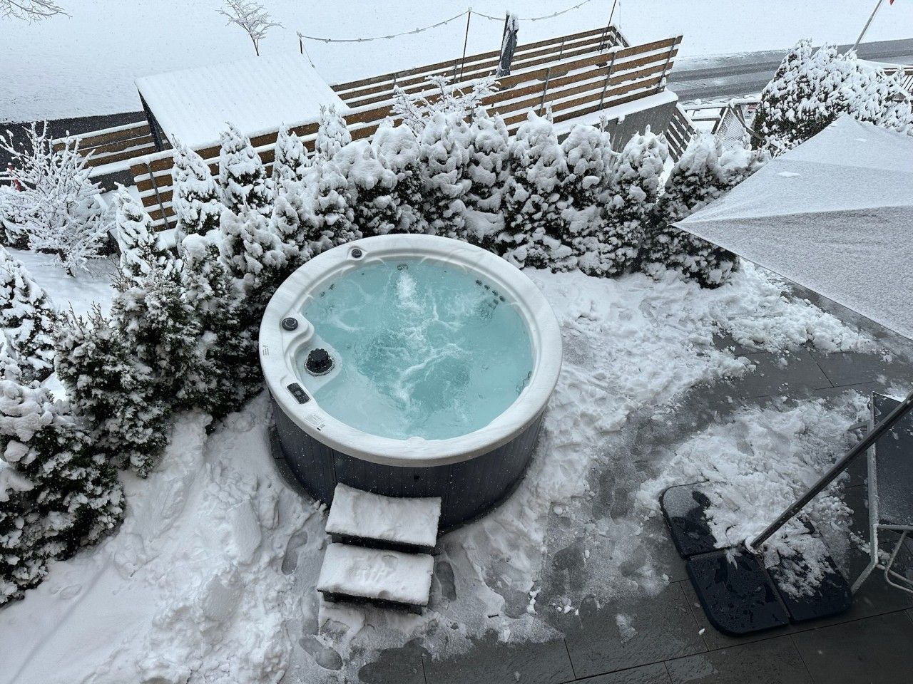 Un jacuzzi rodeado de arbustos cubiertos de nieve y una terraza de madera.