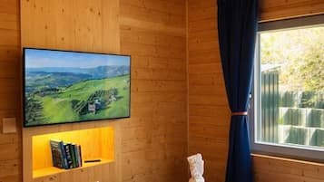 Une pièce aux murs lambrés, avec un lit, un téléviseur fixé au mur et une fenêtre avec des rideaux.