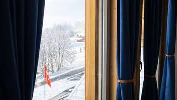Quarto com uma janela ampla, cortinas e vista para uma paisagem nevada com uma bandeira.