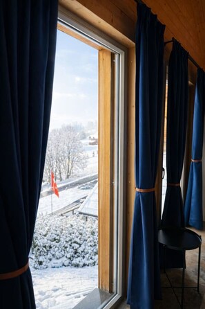 Et værelse med et stort vindue, gardiner og udsigt til et sneklædt landskab med et flag.