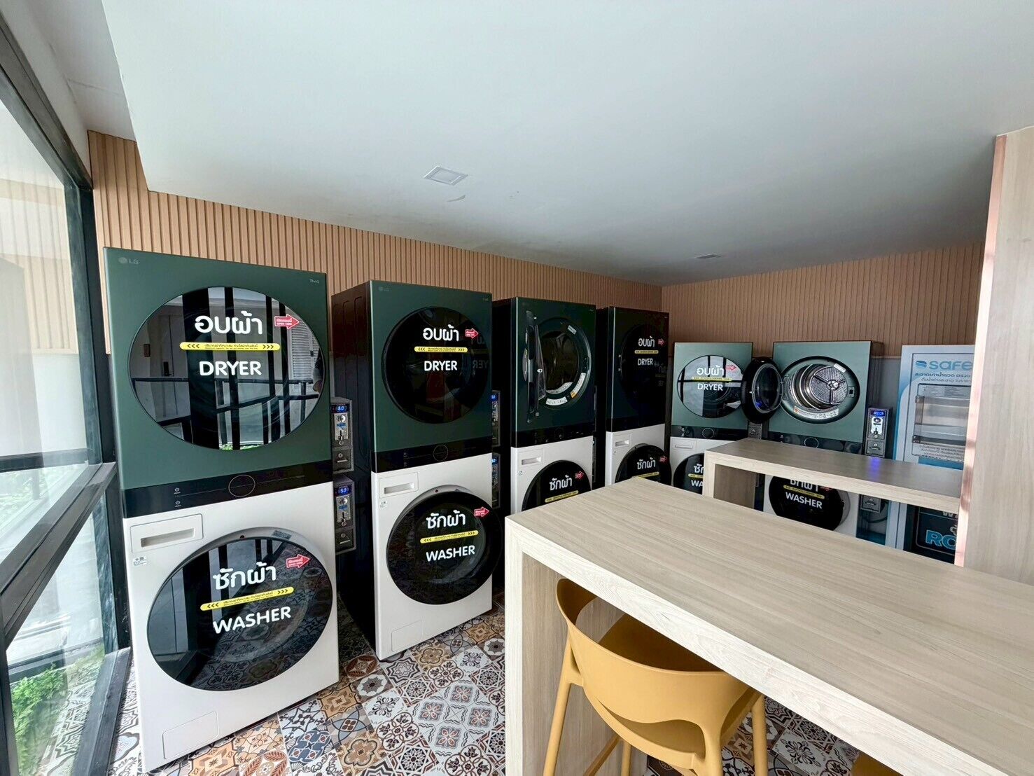 A laundry facility with multiple washing machines and dryers, a wooden table, and a yellow chair.