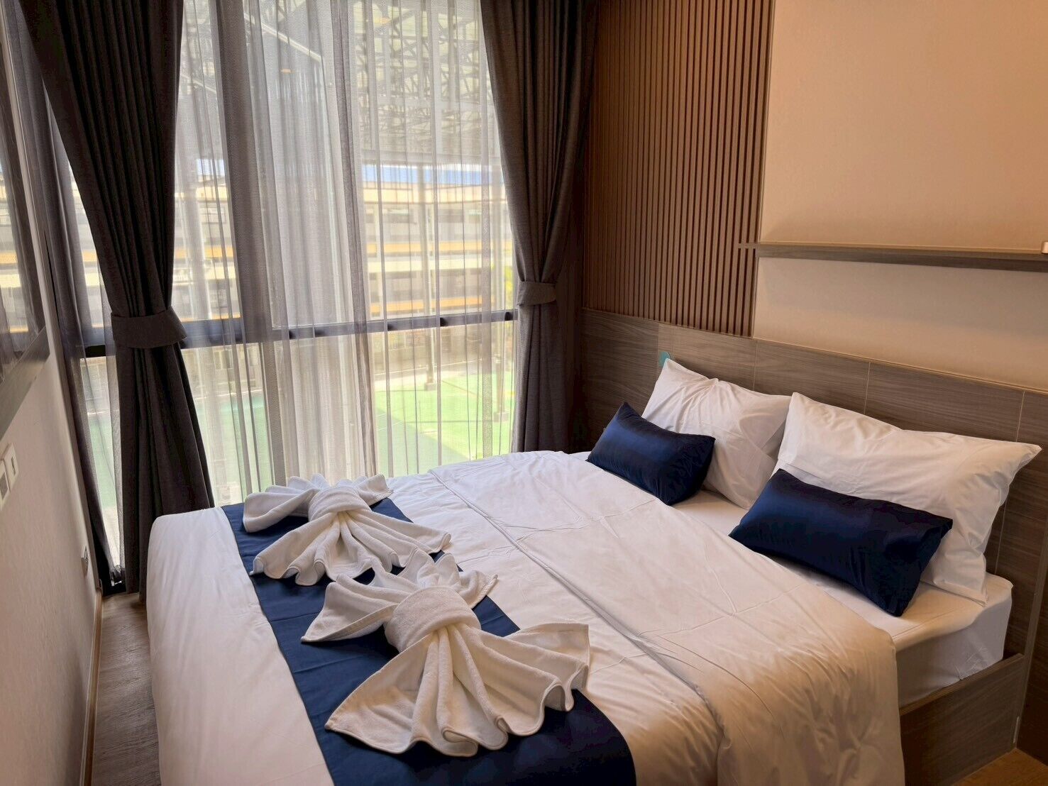 A hotel room with a bed, curtains, and a view of the outside.