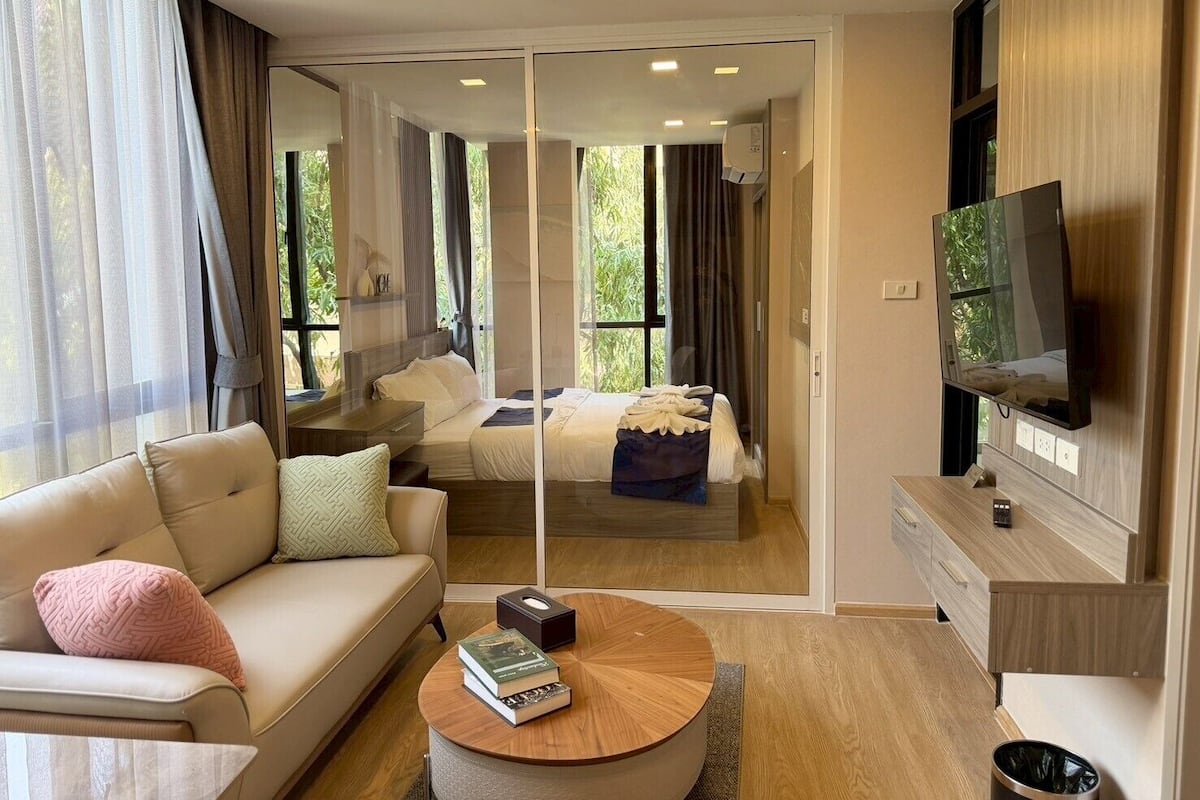 Habitación de hotel moderna con sofá, una mesita redonda, televisión y cama con vistas a zonas verdes.