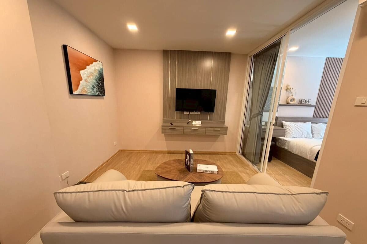 Una habitación de hotel moderna con sofá, televisión de pantalla plana, una mesita de café y una puerta corrediza de cristal que da a un balcón.