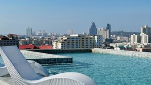 A pool with a white, textured lounge chair, clear water, and a cityscape in the background. - The Iconic (Pattaya)