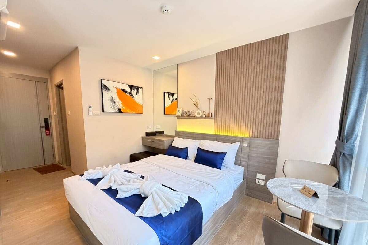 Una habitación de hotel con cama, mesita de noche, silla y una pequeña mesa con un cartel.