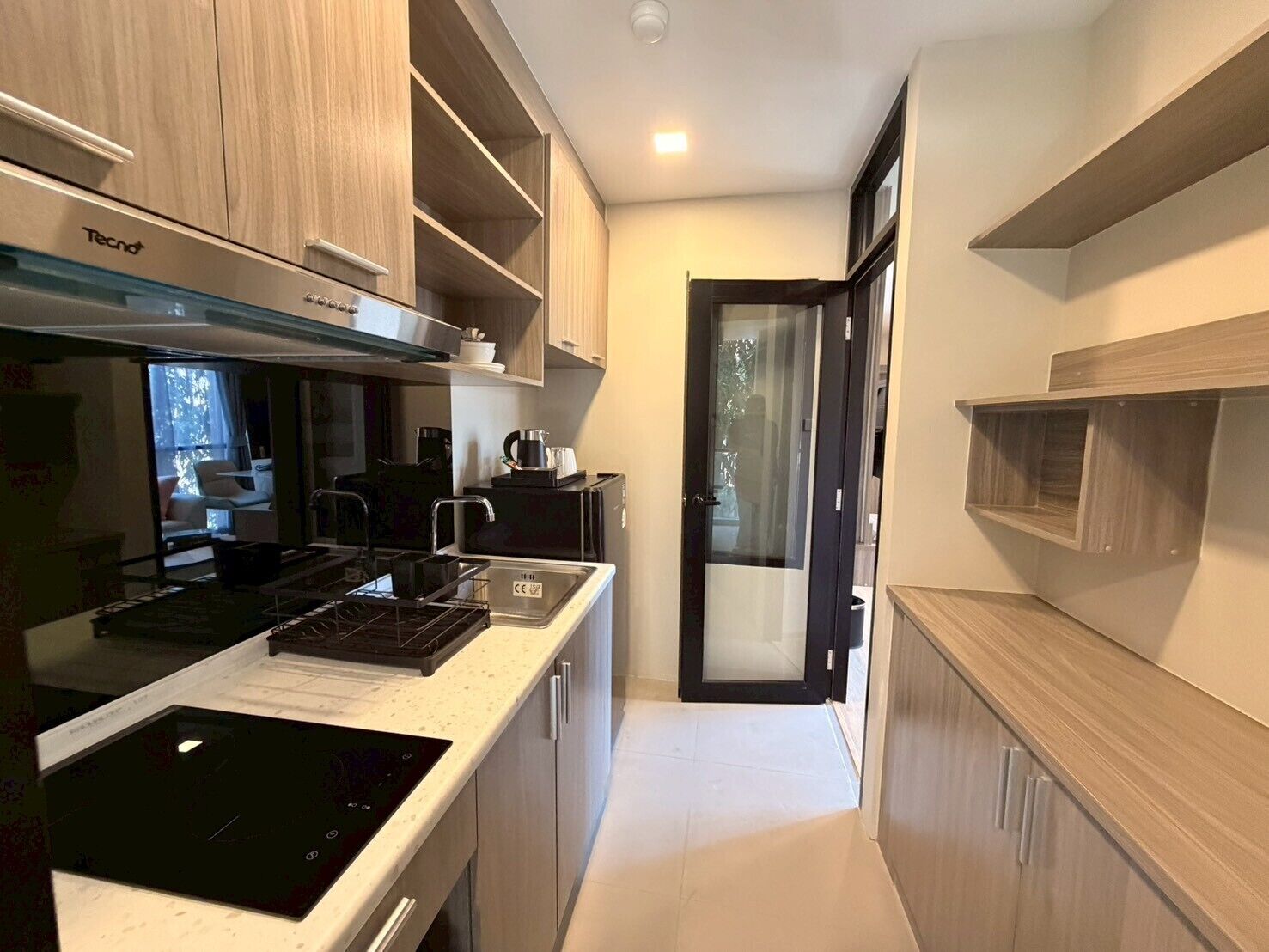A compact kitchen with a Tecno range hood, a black induction cooktop, and a small coffee maker.