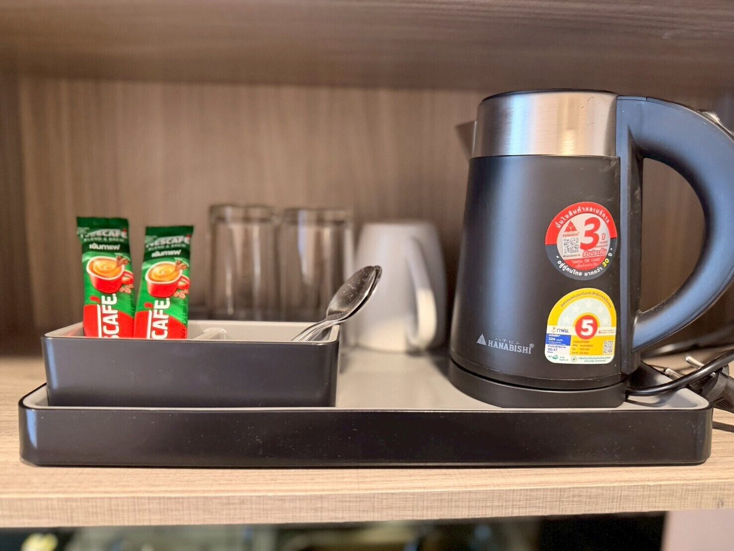 Una moka con un cucchiaino, un vassoio con due capsule di caffè e un bicchiere.
