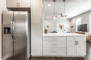 A modern kitchen with a stainless steel refrigerator, white cabinetry, and a central island with drawers. - Lucas Oil Stadium - Modern Downtown Escape (Indianapolis)