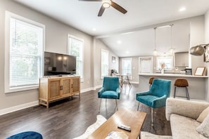 A spacious living room with a television, wooden cabinet, teal chairs, and a coffee table. - Lucas Oil Stadium - Modern Downtown Escape (Indianapolis)