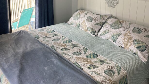 A bedroom with a bed, ceiling fan, artwork, and a view of the outside. - Pelican’s Perch: 3 minute walk to the beach, shops, restaurants and pavilion. (North Myrtle Beach)