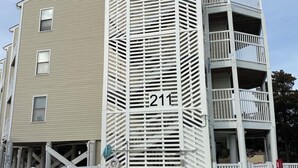 A multi-story building with a distinctive slatted facade, a balcony on the upper floor, and a visible number '211' on the side. - Pelican’s Perch: 3 minute walk to the beach, shops, restaurants and pavilion. (North Myrtle Beach)