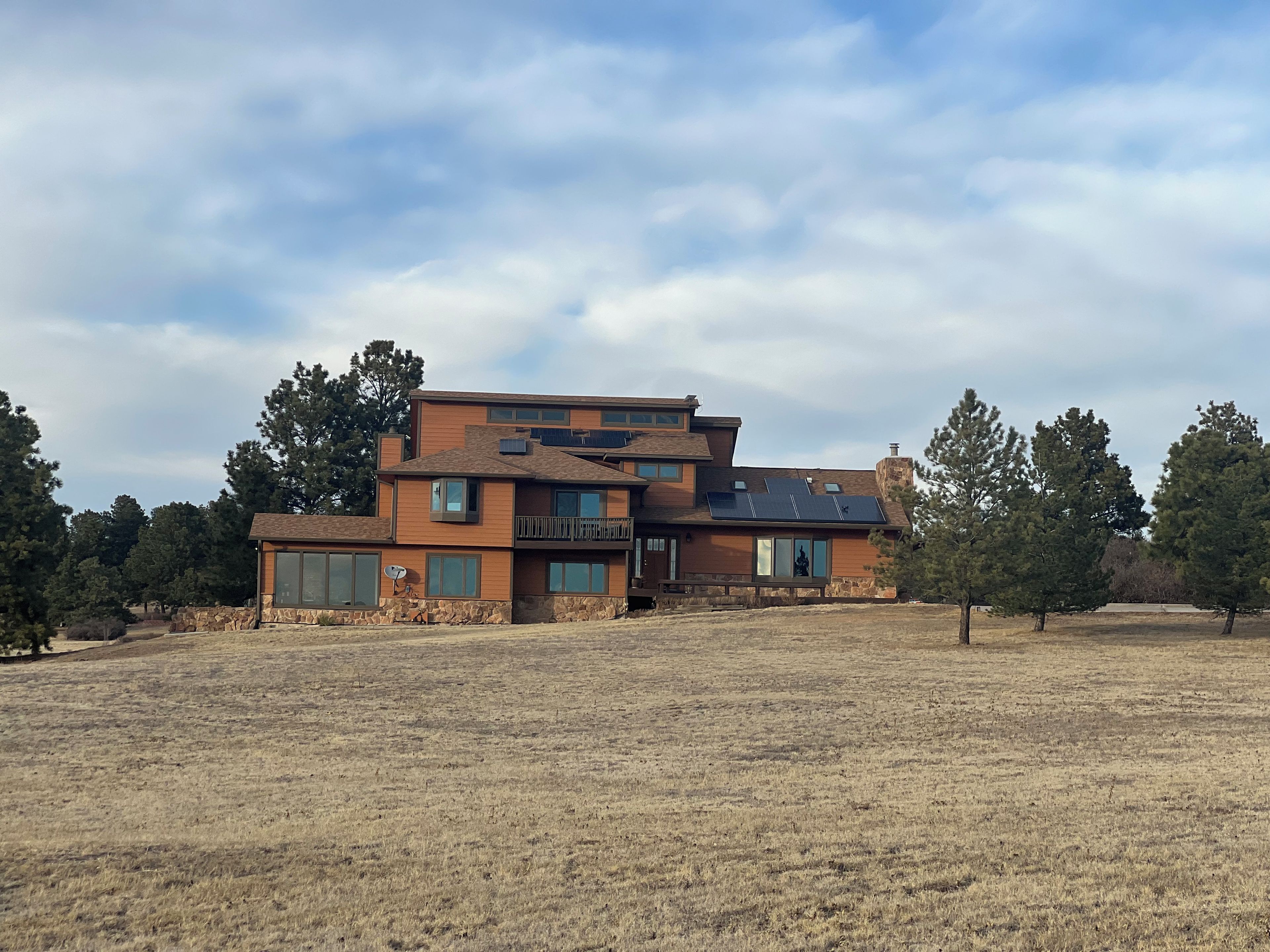 A modern multi-story house with a stone foundation, large windows, and solar panels.