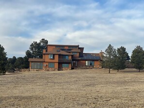 Una casa moderna de varios pisos con base de piedra, ventanas grandes y paneles solares.