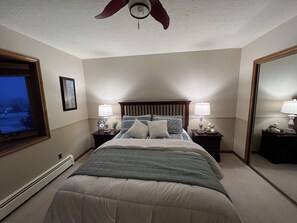 Un dormitorio con una cama, dos mesitas de noche con lámparas, un ventilador de techo, un ventanal con vistas y un espejo.