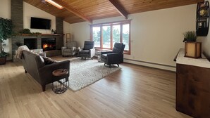 A spacious living room with a fireplace, wooden ceiling, and large windows.