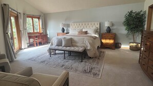 A bedroom with a large bed, bedside tables, a chair, a dresser, and a potted plant.