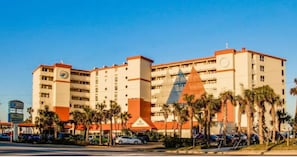 A multi-story hotel with a prominent red and beige color scheme, palm trees in the foreground, and a clear blue sky. - NEW! Cozy Ocean Front Studio in Daytona Beach (Daytona Beach)