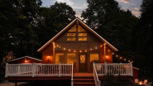 A cabin with a wooden exterior, a front porch with white railings, and a staircase leading to the entrance. - Pocono Basecamp | Hot Tub Chalet + Big Game Room (Tunkhannock Township)