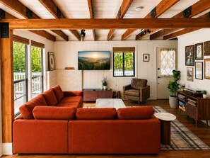 Ein Wohnzimmer mit Ecksofa, Couchtisch, Sessel, Fernseher und Bücherregal.