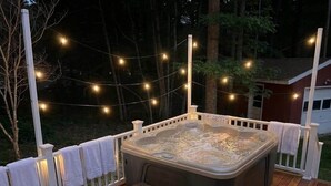 A hot tub on a wooden deck with string lights, surrounded by a white fence. - Pocono Basecamp | Hot Tub Chalet + Big Game Room (Tunkhannock Township)