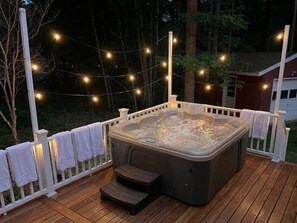 Ein Whirlpool auf einer Holzterrasse mit Lichterketten, umgeben von einem weißen Zaun.