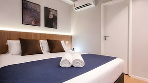 A neatly made bed with a blue bedspread, white pillows, and rolled towels. - Studio Elegance Next Pamplona (São Paulo)