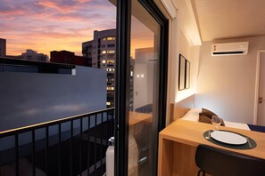A modern room with a balcony, a dining area with a table and chairs, and a view of the cityscape at sunset. - Studio Elegance Next Pamplona (São Paulo)