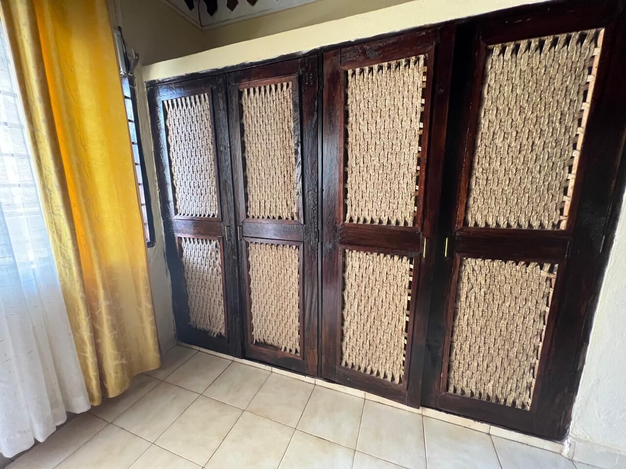 A room with a large window, a curtain, and a tiled floor.